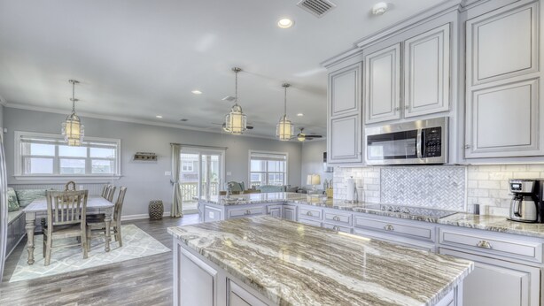 A spacious kitchen with marble countertops, white cabinetry, and pendant lighting. - Blessed at the Beach - Gulf View, Heated Pool and Jacuzzi. (Dauphin Island)