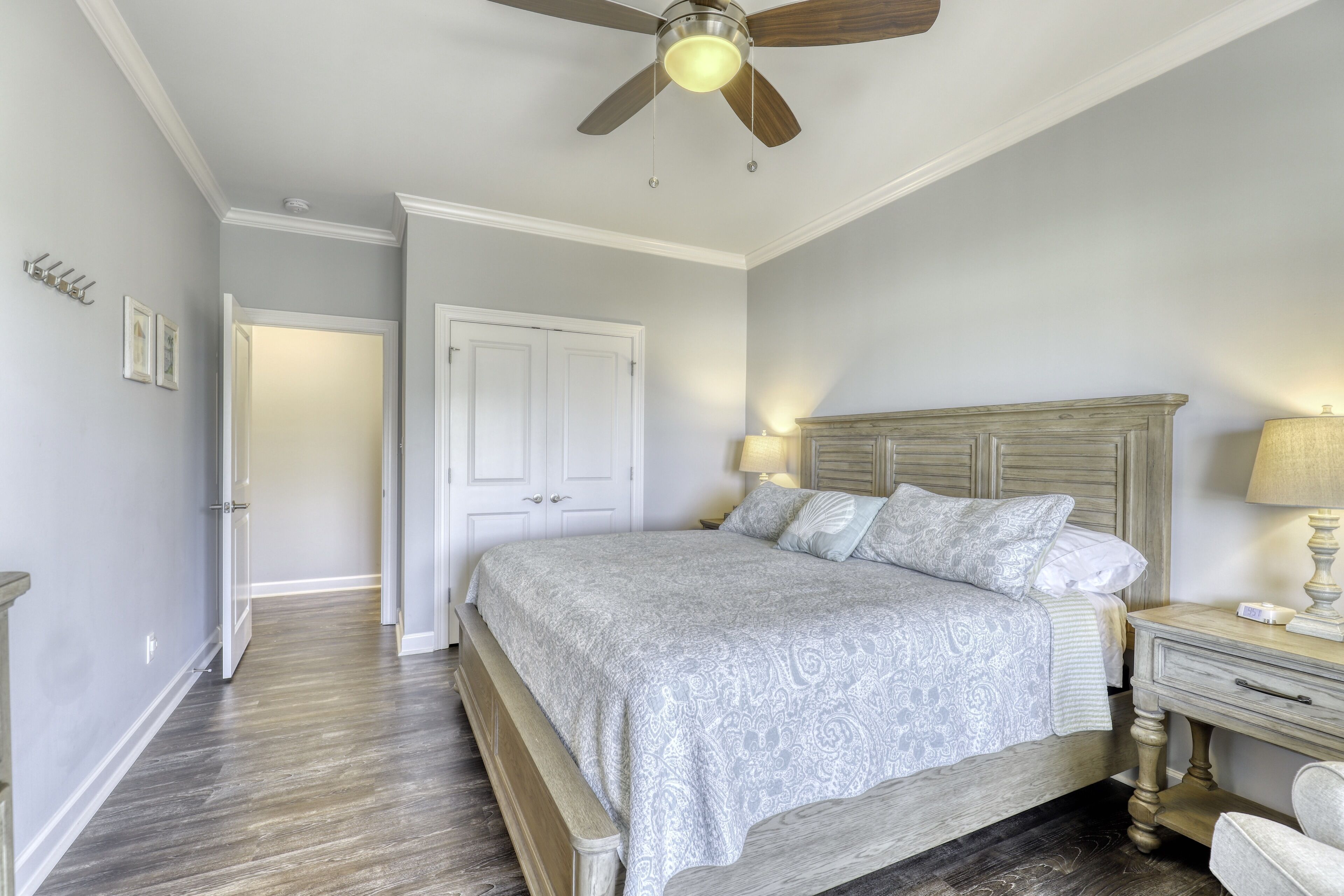 Une chambre à coucher avec un lit, une table de chevet, une lampe, un ventilateur de plafond et une porte.