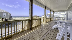 A wooden deck with a railing overlooking a beach, featuring a covered area with tables and chairs. - Blessed at the Beach - Gulf View, Heated Pool and Jacuzzi. (Dauphin Island)