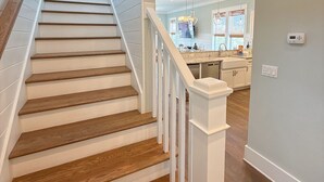 Un escalier avec des marches en bois et des rampes blanches menant à un espace cuisine doté d’un comptoir et d’armoires.