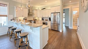 Une cuisine moderne avec des meubles blancs, un grand îlot central doté de tabourets, des appareils en acier inoxydable et un éclairage suspendu.
