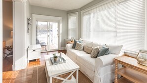 A living room with a white sofa, a coffee table, and a wooden side table. There is a door leading to a balcony.