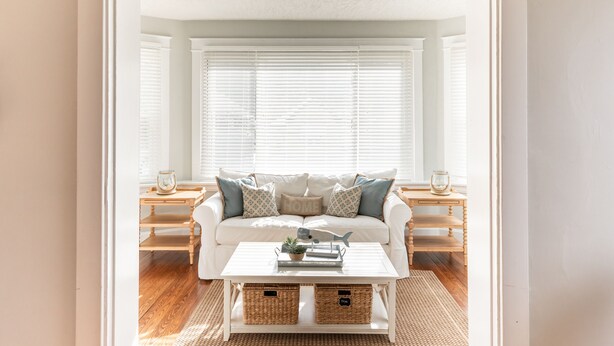 A cozy living room with a white sofa, a coffee table, and a window with blinds.