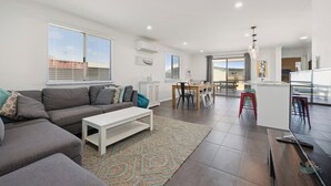 A modern living room with a grey sofa, a white coffee table, and a patterned rug. There is a dining area with a table and chairs, and a kitchen with a bar area. - Seagulls is the ultimate seaside escape! (Lancelin)