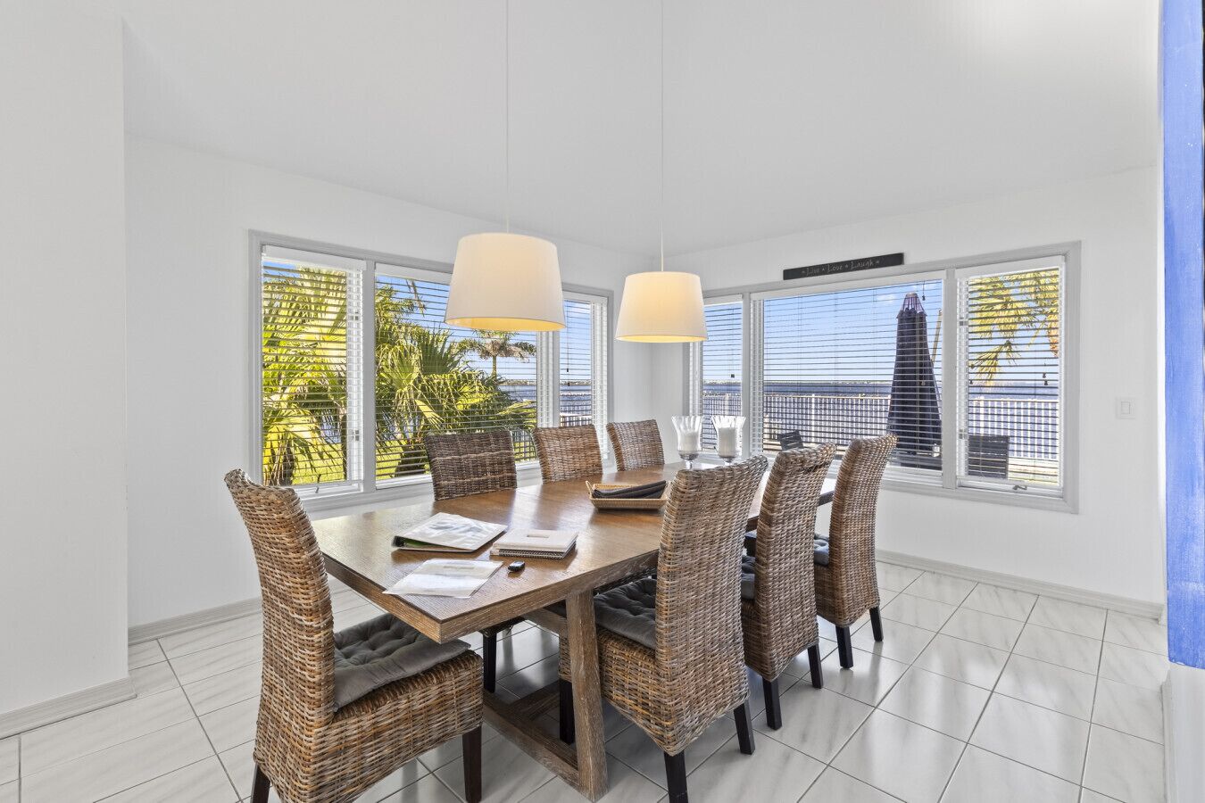 A dining area with a large table, wicker chairs, and two pendant lights.