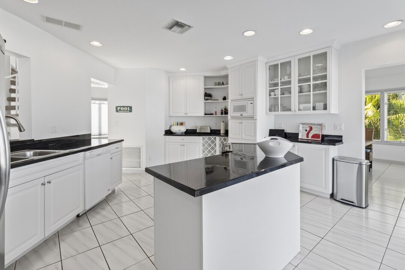A modern kitchen with white cabinetry, a black countertop island, and a stainless steel trash can.