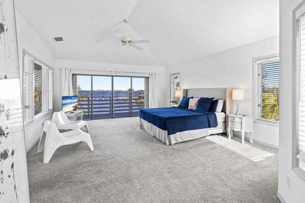 A bedroom with a large bed, a ceiling fan, a TV, and a view of the ocean through the sliding glass doors. - Luxury Pool Villa Located Directly On The River In A Fantastic Location (Cape Coral)