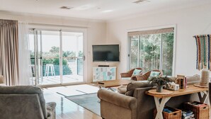 A modern living room with a sofa, a dining table, and a TV. - Private Luxury Couples Retreat The Bathhouse at Aldinga Bay. Sunsets, BeachWalks (Sellicks Beach)