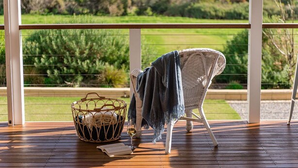 A wicker chair with a blue towel on a wooden deck overlooking a green landscape. - Private Luxury Couples Retreat The Bathhouse at Aldinga Bay. Sunsets, BeachWalks (Sellicks Beach)