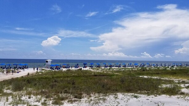 A beach with blue umbrellas and lounge chairs, a lifeguard tower, and a clear sky. - Comfy and Cozy 5 min walk to the Gulf in Historic District (Gulfport)