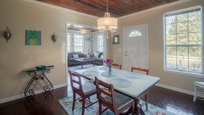A dining area with a wooden ceiling, a chandelier, a table with chairs, and a view of the outdoors through large windows. - Comfy and Cozy 5 min walk to the Gulf in Historic District (Gulfport)
