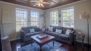 A living room with two couches, a coffee table, a ceiling fan, and large windows. - Comfy and Cozy 5 min walk to the Gulf in Historic District (Gulfport)