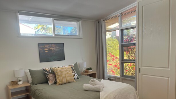 Un dormitorio con cama, mesita de noche, ventana y puerta.