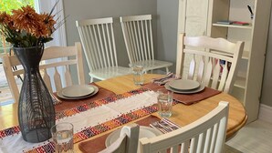 A dining room with a wooden table, white chairs, a vase with flowers, and a painting on the wall. - Idyllic Location - Walk to Town and Beaches (South Haven)