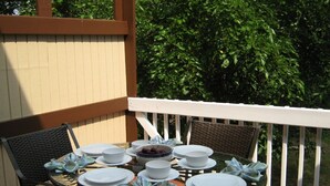 A round table set for four with white plates and a bowl of fruit, surrounded by wicker chairs on a wooden deck with a white railing. - Idyllic Location - Walk to Town and Beaches (South Haven)