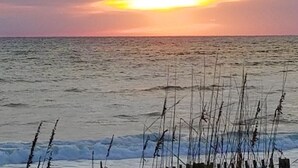 A sunset over the ocean with waves and reeds in the foreground. - At Last: Oceanfront Condo, YMCA Membership (Kill Devil Hills)