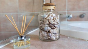A bathroom with a glass jar filled with seashells and reed sticks, and a small glass bottle with reed sticks.