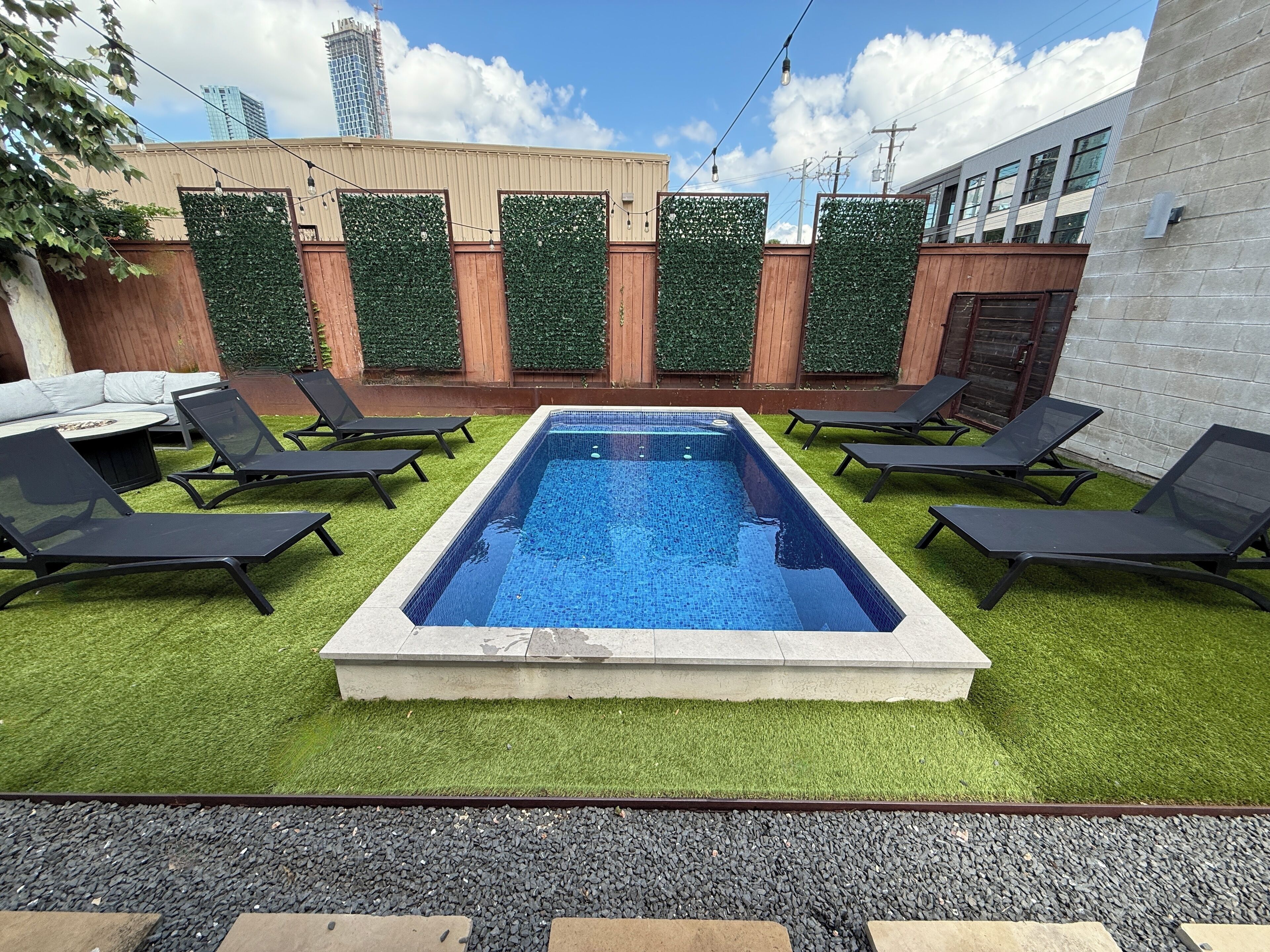 Una piscina rectangular amb gandules negres al voltant, envoltada d'herba artificial i una paret decorativa amb vegetació verda.