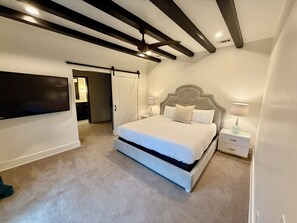 Une chambre avec un grand lit, un téléviseur fixé au mur et un ventilateur de plafond.