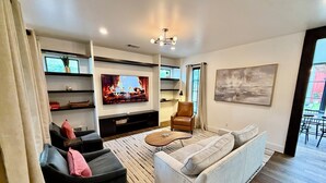 Een moderne woonkamer met een flatscreen-televisie, een leren fauteuil, een bank en een salontafel.