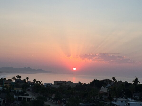 Solnedgang ved kysten med bygninger i forgrunden.