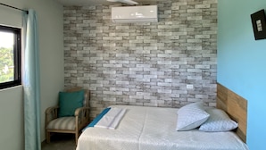 A bedroom with a brick-patterned wall, a ceiling fan, a bed with white bedding, a wooden chair, and a window with curtains. -  Near the best Surf beaches in San Jose del Cabo! (San José del Cabo)