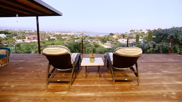 A wooden deck with two wicker chairs and a small table, overlooking a scenic landscape with buildings and greenery. -  Near the best Surf beaches in San Jose del Cabo! (San José del Cabo)