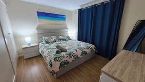 A bedroom with a bed, nightstands, a lamp, a painting, and a curtain.