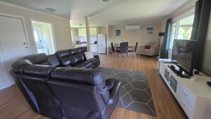 A modern living room with a leather sofa, a dining area with a table and chairs, and a TV on a stand. - Family friendly Smiths Beach Retreat (Smiths Beach)