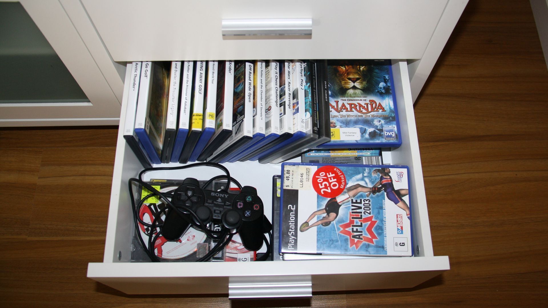 A drawer with video games, a PlayStation 2 console, controllers, and a DVD.