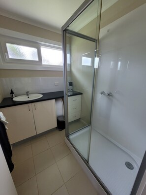 A modern bathroom with a glass shower enclosure, a sink with a mirror, and a window above the sink.