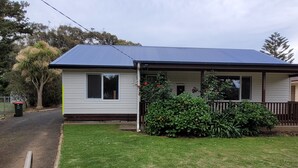 A single-story house with a blue roof, a front porch, and a small garden with red flowers. - Family friendly Smiths Beach Retreat (Smiths Beach)