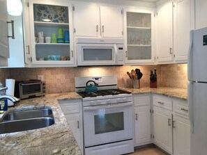 A kitchen with white cabinets, a microwave, a stove, and a sink.