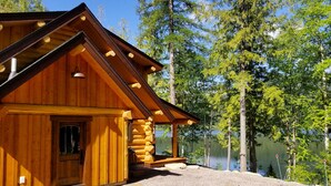 A wooden cabin with a sloped roof, a front door, and a porch with logs. - A Serene Lake Front Cabin Minutes from West Glacier National Park (Columbia Falls)