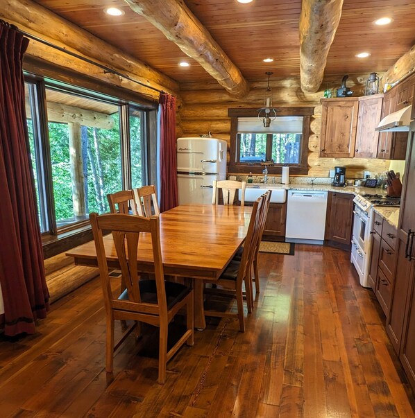 Interior de una cabaña de madera con una mesa de comedor, sillas, un refrigerador, un lavamanos y una estufa.