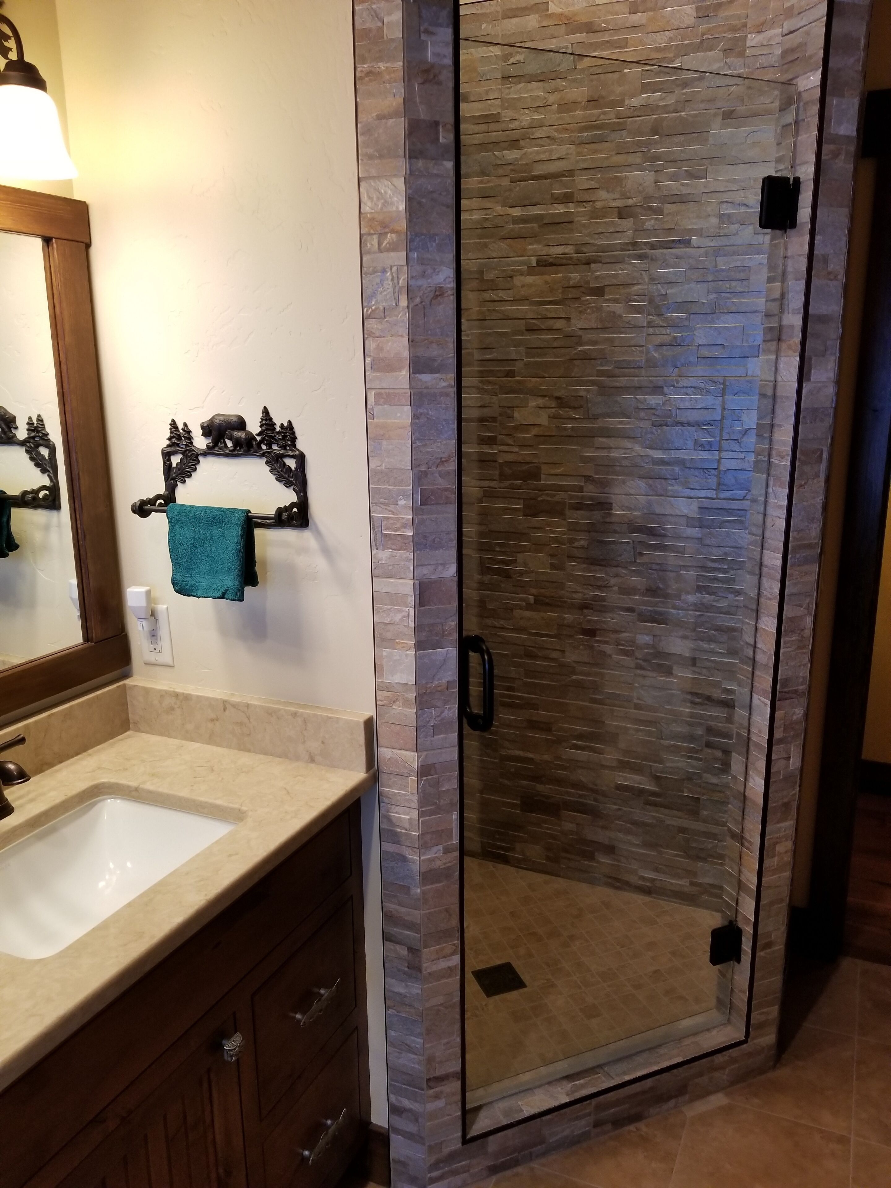 Une salle de bain avec une douche à parois de verre, un lavabo et un miroir orné d’un motif d’ours.