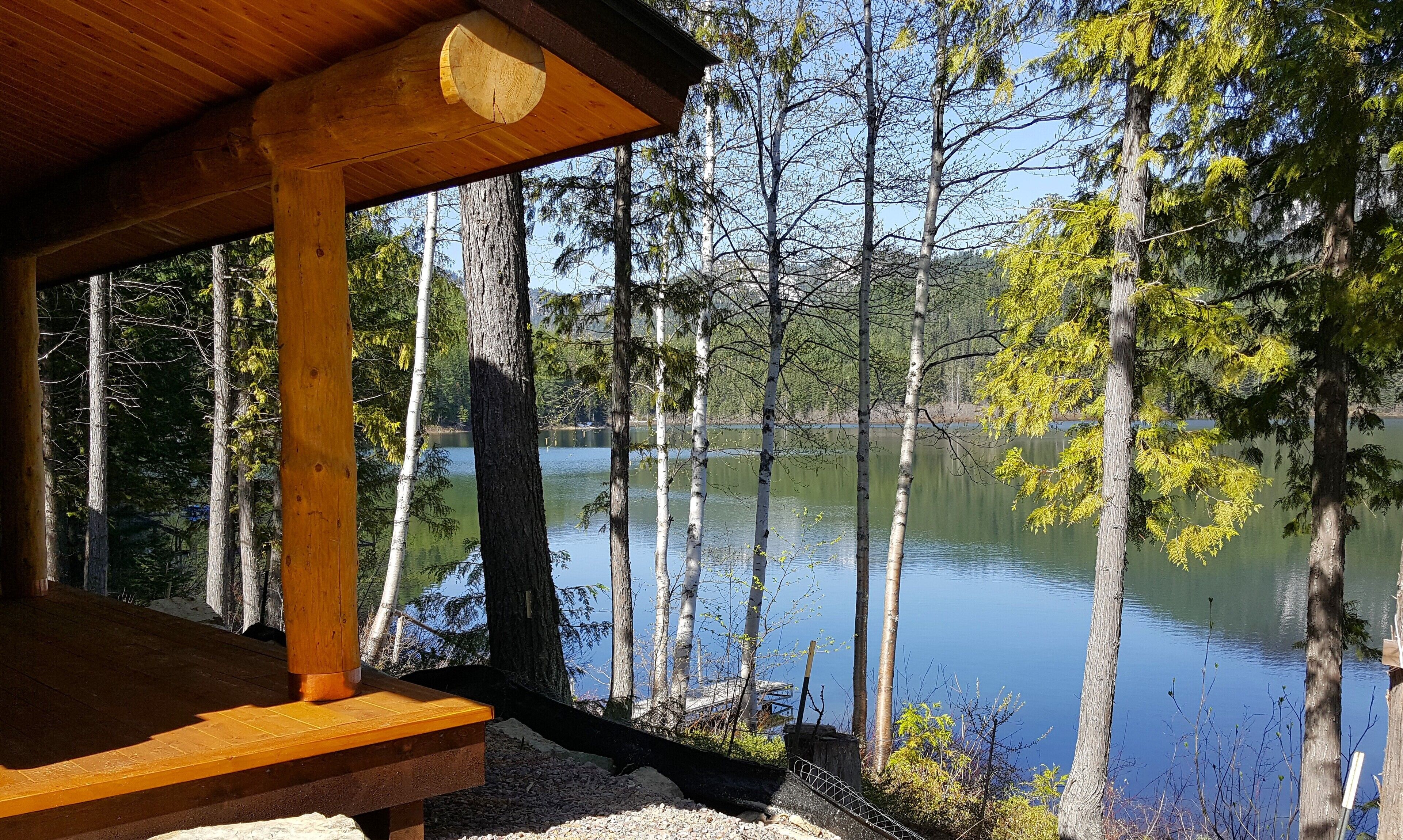 A wooden deck with a view of a calm lake surrounded by trees.