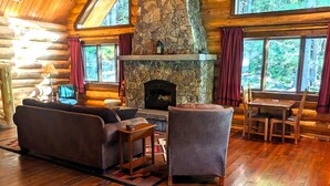 A log cabin interior with a stone fireplace, wooden furniture, and large windows. - A Serene Lake Front Cabin Minutes from West Glacier National Park (Columbia Falls)