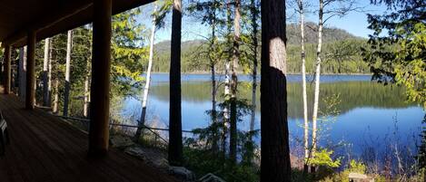 Une terrasse en bois, dotée de chaises, qui offre une vue sur un lac paisible, entouré d’arbres.