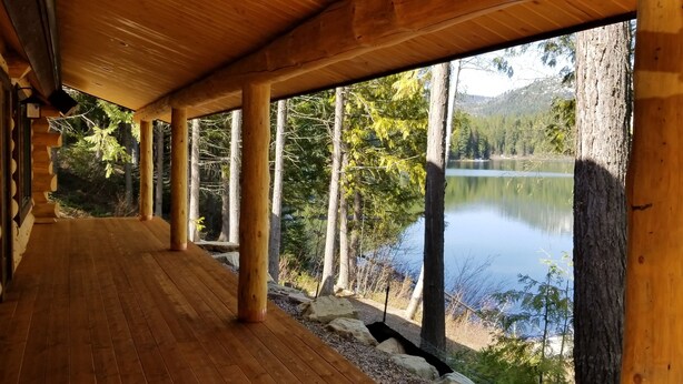 A wooden deck with large windows overlooking a lake and forest. - A Serene Lake Front Cabin Minutes from West Glacier National Park (Columbia Falls)