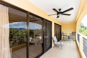 A balcony with a ceiling fan, glass doors, and a view of greenery and buildings. - Newly Remodeled Flamingo Condo with Sweeping Ocean Views, Spacious Terrace & Walkable Location (Playa Flamingo)