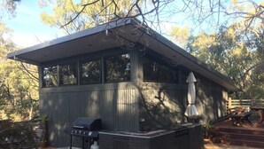 A modern outdoor kitchen with a grill and seating area, surrounded by a wooden deck and trees. - Janaza Retreat right in the middle of Halls Gap township. Pet friendly. (Halls Gap)