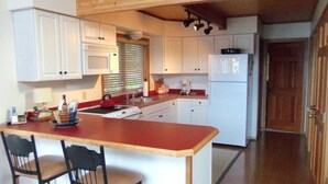 Una cocina con armarios blancos, encimera roja, estufa, fregadero y refrigerador. Hay dos sillas en la isla de la cocina.