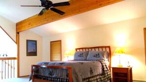 Un dormitorio con una cama, dos lámparas de noche, un ventilador de techo y un cabecero de madera.