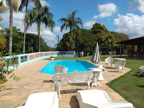 A swimming pool with white chairs and a table, surrounded by a brick wall and palm trees. - Chác.Happiness 19 992317334Socorro (Wi-Fi) (Socorro)