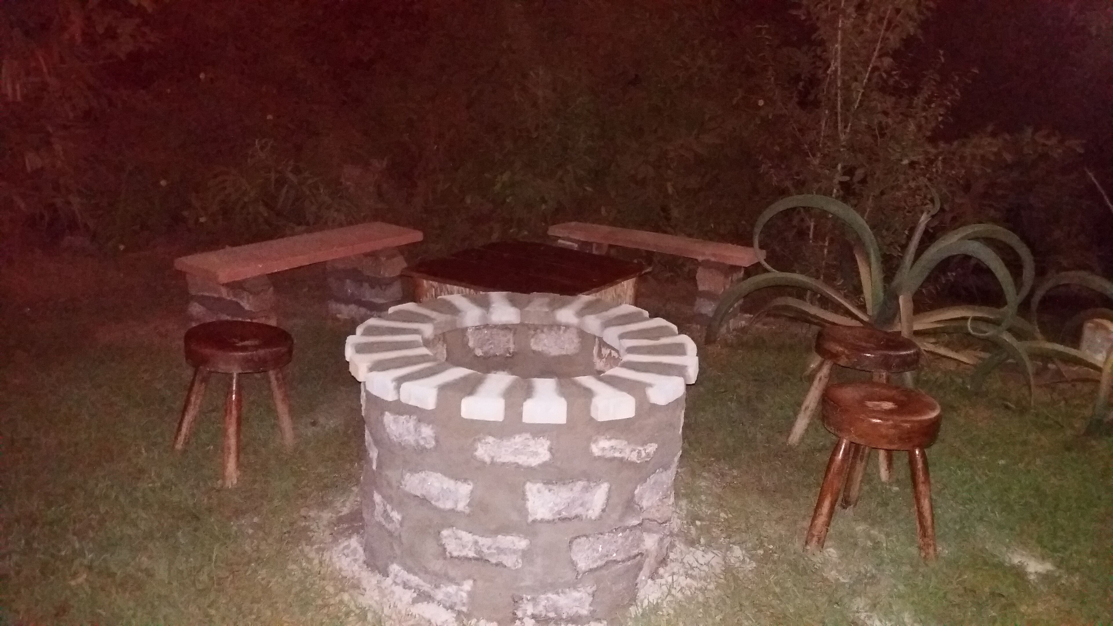 A stone fire pit with a circular seating area, two wooden stools, and a wooden table.
