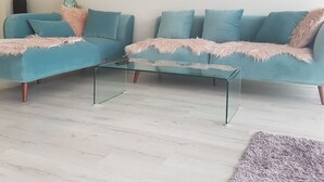 Un salon moderne avec un canapé turquoise, une table basse en verre et un tapis moelleux.