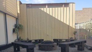 Un espace extérieur aménagé avec deux bancs, un foyer en pierre et une clôture en métal.