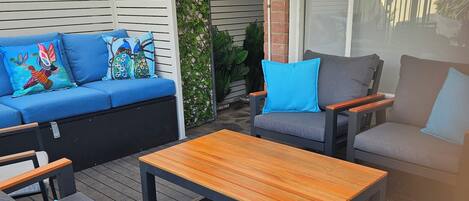 Un área de patio al aire libre con un sofá, dos sillones y una mesa de madera.