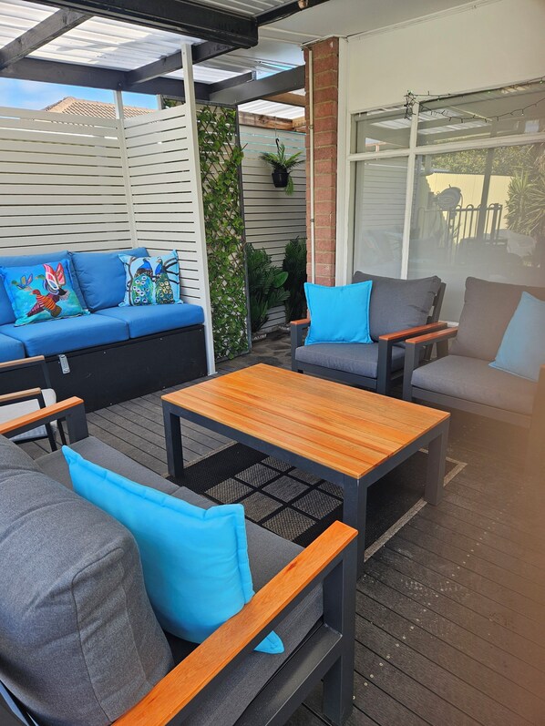 An outdoor patio area with a sofa, two armchairs, and a wooden table.